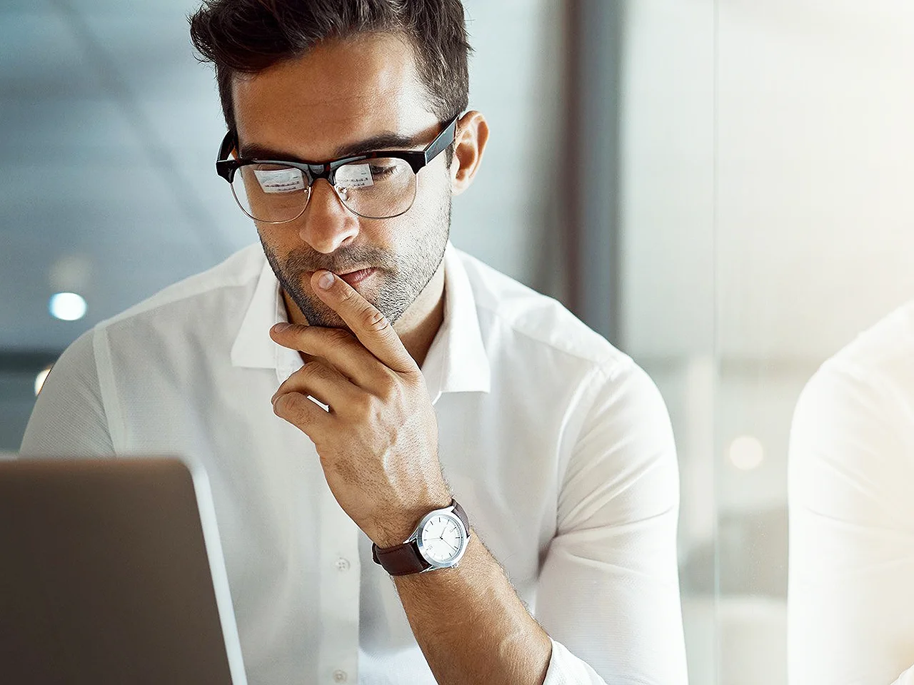 Young businessman looking thoughtful while working on his laptop in the office